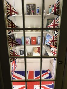 View of a cabinet of shelves full of books and mugs surrounded by decorative Union Jack flags.