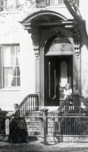 An entry with several stairs and carved railings leading to double doors under a curved awning supported by scrolled corbels.