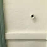 A small tube with a hole in it sticking out of a plain white wall above a white chair rail.