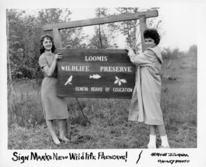 wooden sign for the Loomis Wildlife Preserve being hung by two unidentified girls.