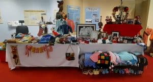 Two tables in a gallery with displays of handcrafted items like sweathers and hangings.