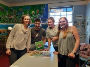 four people gathering around a table posing with a completed jigsaw puzzle