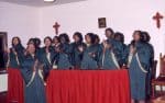 A gospel choir dressed in green robes singing and clapping.