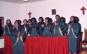 A gospel choir dressed in green robes singing and clapping.