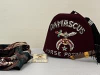 Several men's ties and a maroon hat with the words "Damascus horse parade" in spangles and a tassel on top.