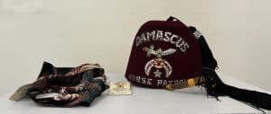 Several men's ties and a maroon hat with the words "Damascus horse parade" in spangles and a tassel on top.