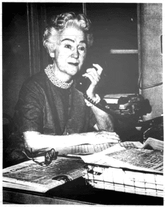 A middle aged woman sitting at a desk talking on a landline phone.