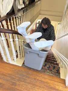 Person moving items in a plastic tub down a flight of stairs at the Geneva History Museum