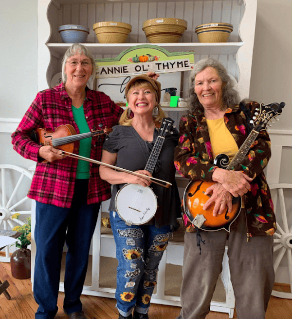 Three woman posing with their instruments, a violin, banjo and mandolin.