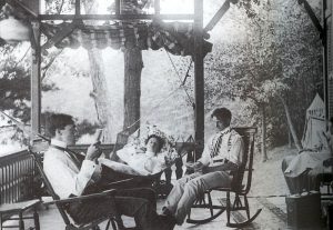 three people sitting on cottage porch early 1900s during the summer 