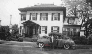 A woman standing along side a car in front of a house