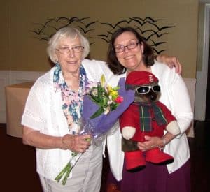 One woman holding flowers and another woman holding a teddy bear