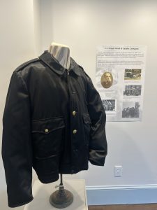 A black leather firefighters jacket on a stand in front of an exhibit panel headed CJ Folger Hook & Ladder Company.