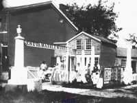 The yard outside Geneva Marble Works where a group of men in aprons and work clothes stand among the monuments and gravestones there.