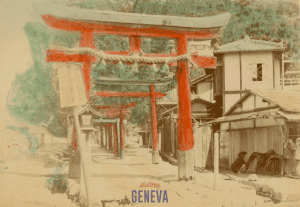 A sequence of Japanese torii gates leading down a road next to a building.