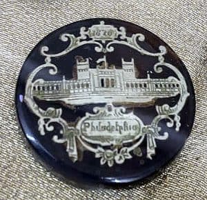 black button with silver image of building 1876