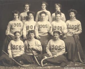 Female field hockey players in sweaters and long skirts.