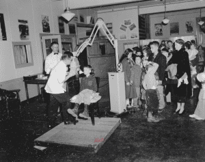 One child sitting in a dentist's chair with a group of children in the background