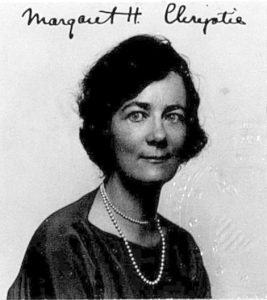 A headshot of a middle-aged woman wearing a dark shirt and pearls.