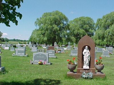 View across a cemetery with a large monument in the foreground containing a statue of the Sacred Heart in an stone arch.