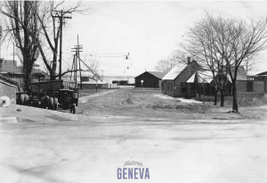 View down a dirt road with low buildings along it toward a lake.